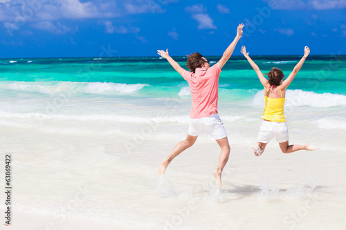 Young couple in bright clothes jumping on the beach