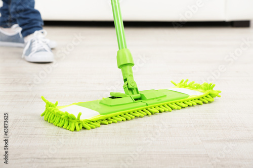 Woman with mop cleaning wooden floor from dust