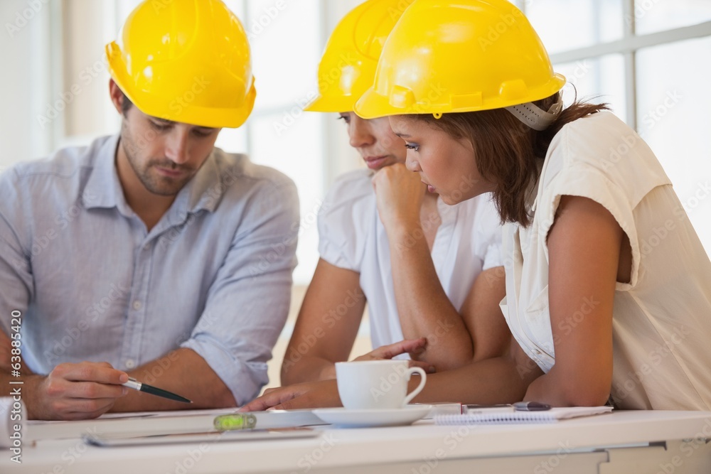 Architects in yellow helmets working on blueprints Architects in yellow helmets working on blueprints