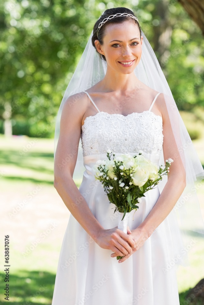 Bride holding bouquet in park - obrazy, fototapety, plakaty 