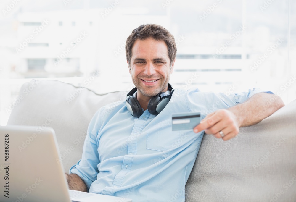 Fototapeta premium Happy handsome man sitting on sofa online shopping with laptop