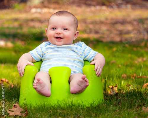 Happy infant baby boy using training seat photo