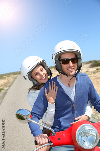Cheerful couple riding red moto on island