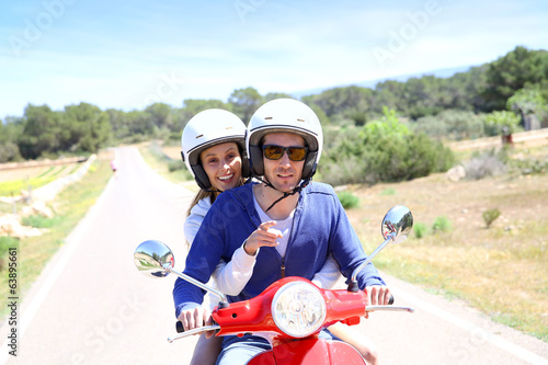 Cheerful couple riding red moto on island