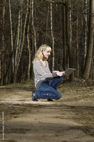 Woman with laptop sits on a footpath in wood