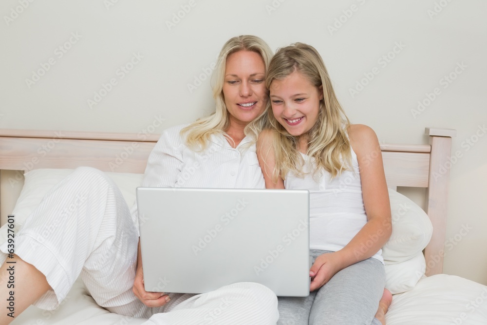 Smiling mother and daughter using laptop in bed Smiling mother and daughter using laptop in bed