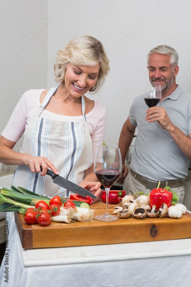 Man with wine glass and woman chopping vegetables in kitchen Man with wine glass and woman chopping vegetables in kitchen