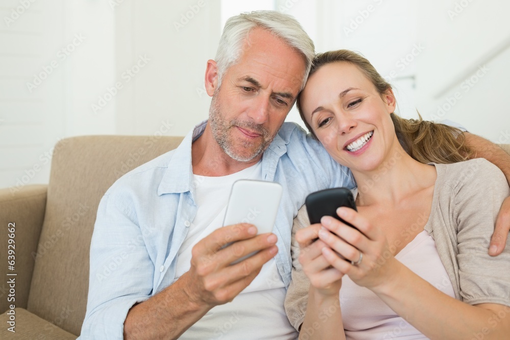Happy couple sitting on couch texting on their phones Happy couple sitting on couch texting on their phones
