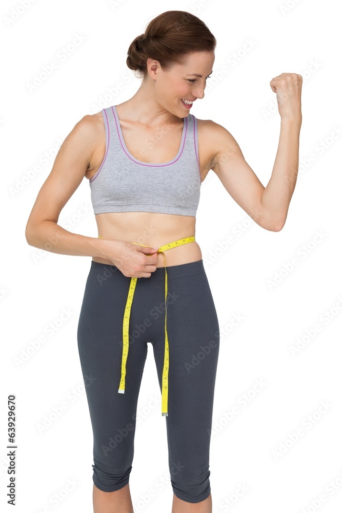 Fit woman measuring waist while flexing muscles Fit woman measuring waist while flexing muscles