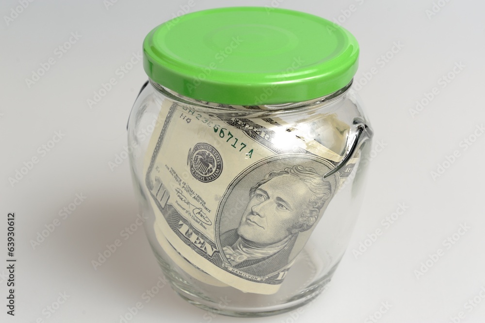 Closed glass jar full of banknotes on gray background Closed glass jar full of banknotes on gray background