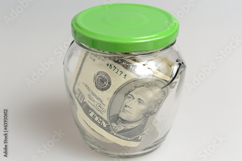 Closed glass jar full of banknotes on gray background