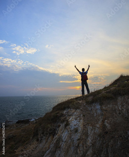 young man standing on rock clift and rising victory hand against