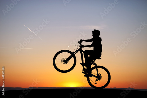 Fototapeta Naklejka Na Ścianę i Meble -  silhouette of boy riding his mountain-bike in sunset