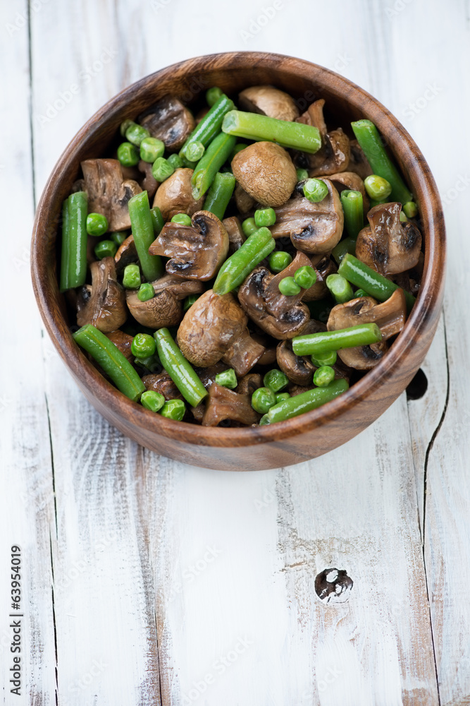 Wooden bowl with roasted champignons, peas and beans, above view Wooden bowl with roasted champignons, peas and beans, above view