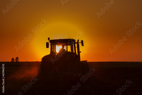 Tractor Plowing in dusk on sunset with crows
