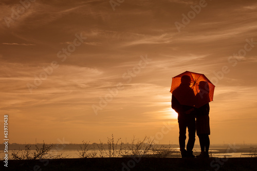 Silhouette of pregnant woman and a man in the sunset under an um