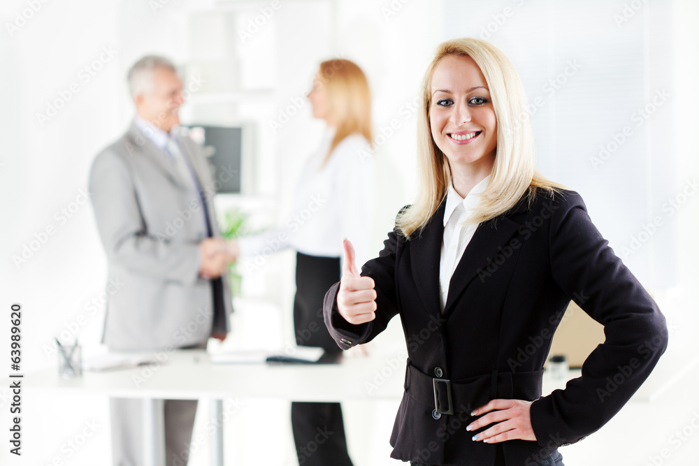 Happy young businesswoman showing thumbs up in the office. Happy young businesswoman showing thumbs up in the office.
