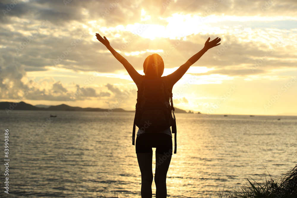Fototapeta premium cheering hiking woman open arms at sunrise seaside
