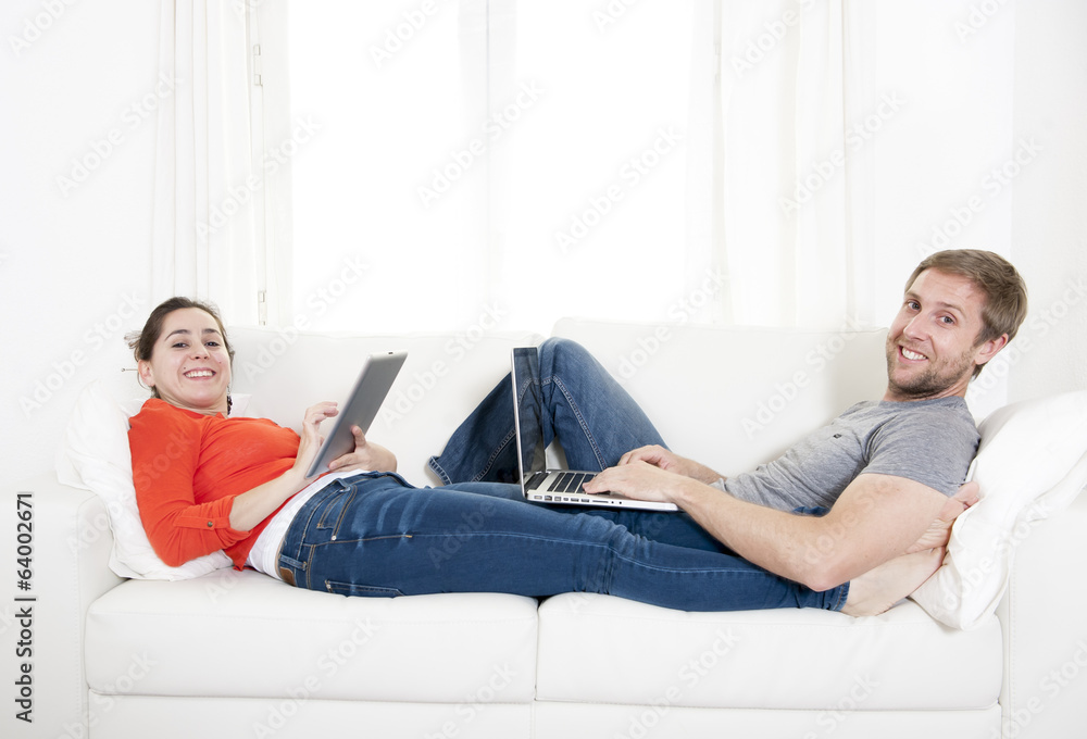 young happy couple working on computer and tablet on sofa