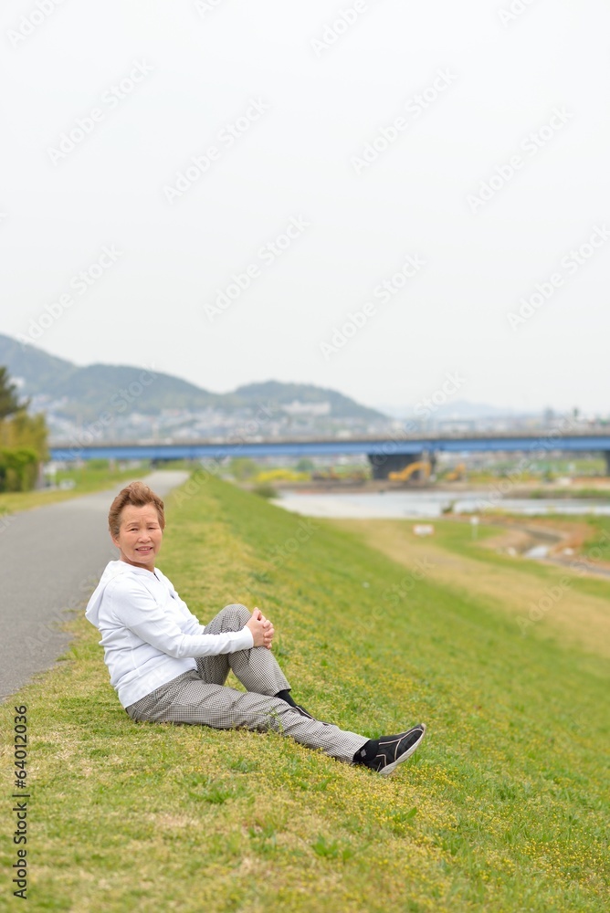 芝生の上に座って準備運動をする高齢のアジア人女性