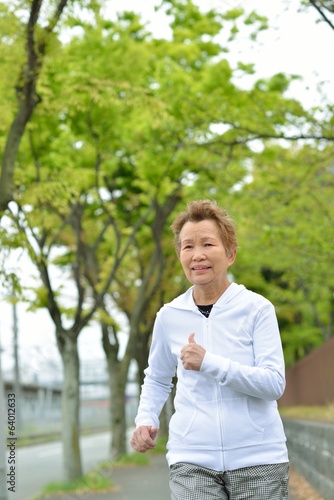 新緑の木々が植えてある歩道を健康のためにジョギングしている高齢のアジア人女性