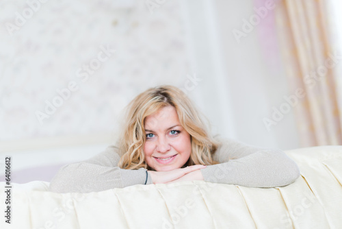  blonde woman with long hair smiling and lying on white bed