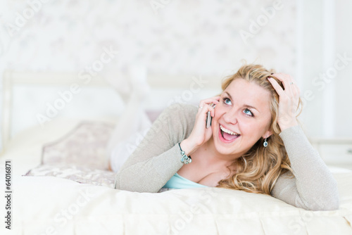 Natural cheerful blonde lying on bed and phoning in bright bedro © Valeri Luzina