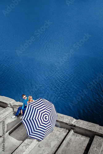 Couple sitting on the pier with beach umbrella on the water on b