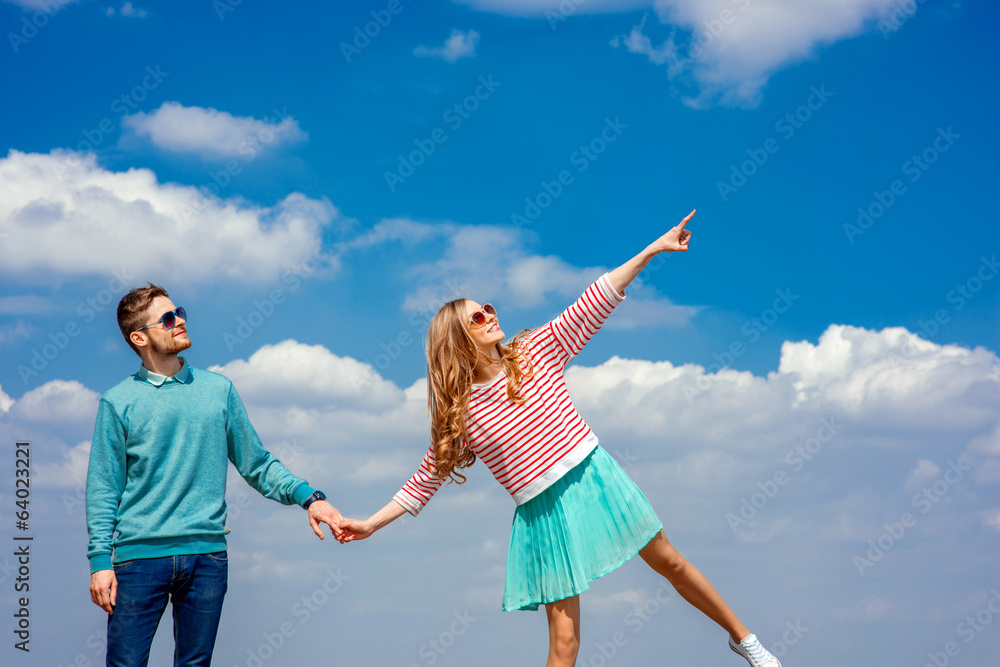 Young couple showing something on the blue cloudy sky Young couple showing something on the blue cloudy sky