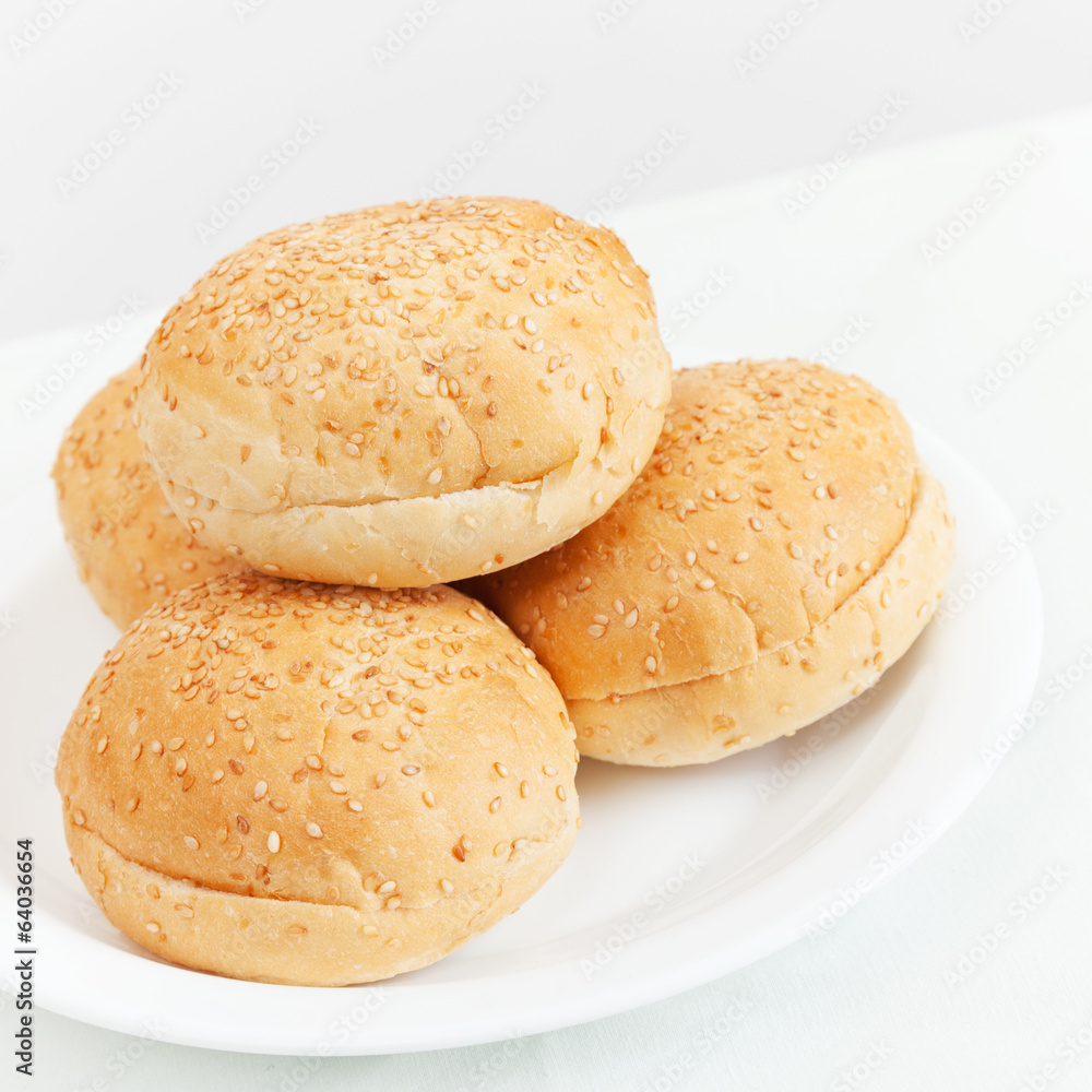 Four small buns for hamburgers lay on white plate Four small buns for hamburgers lay on white plate