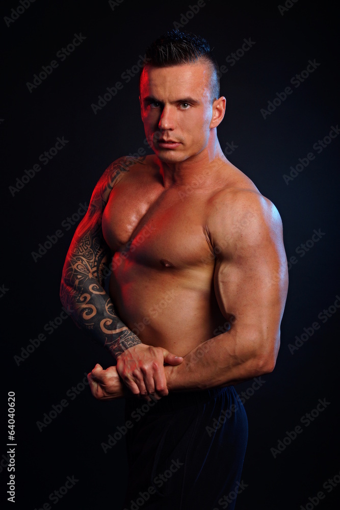 Fototapeta premium Handsome muscular man poses and shows biceps on dark background
