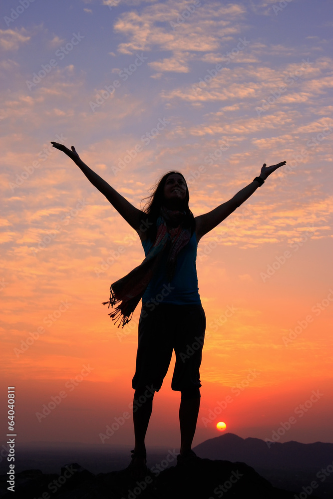 Sillouetted woman with her arms up at sunset on top of the hill,