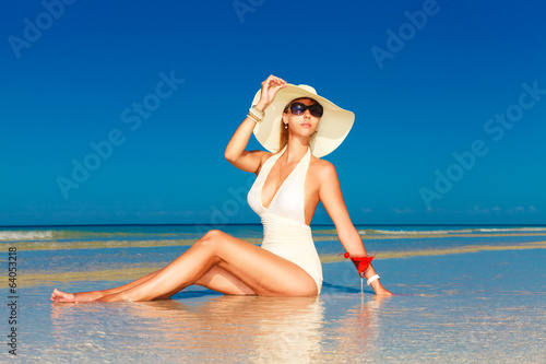 young woman in straw hat sitting at the tropical beach and enjoy