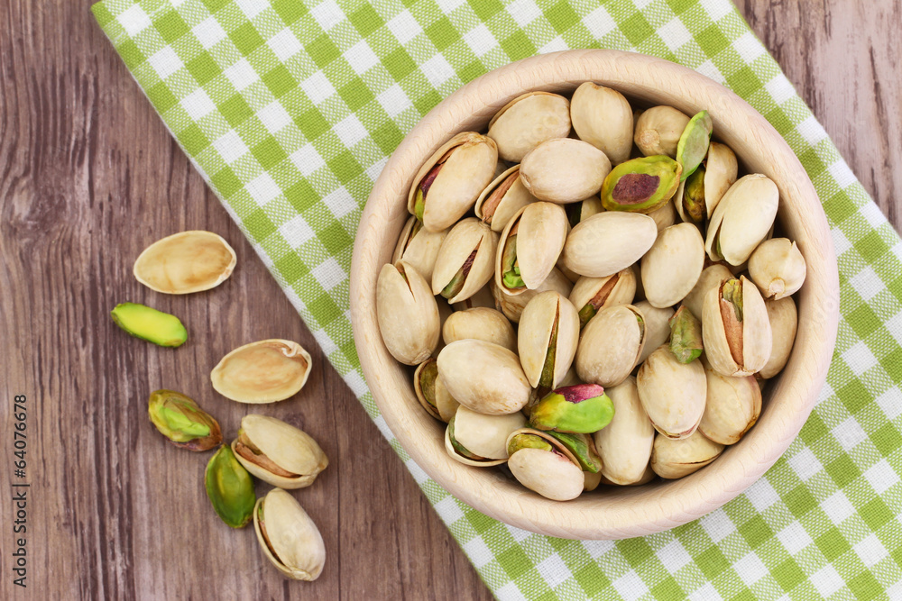 Pistachio nuts in wooden bowl on checkered cloth