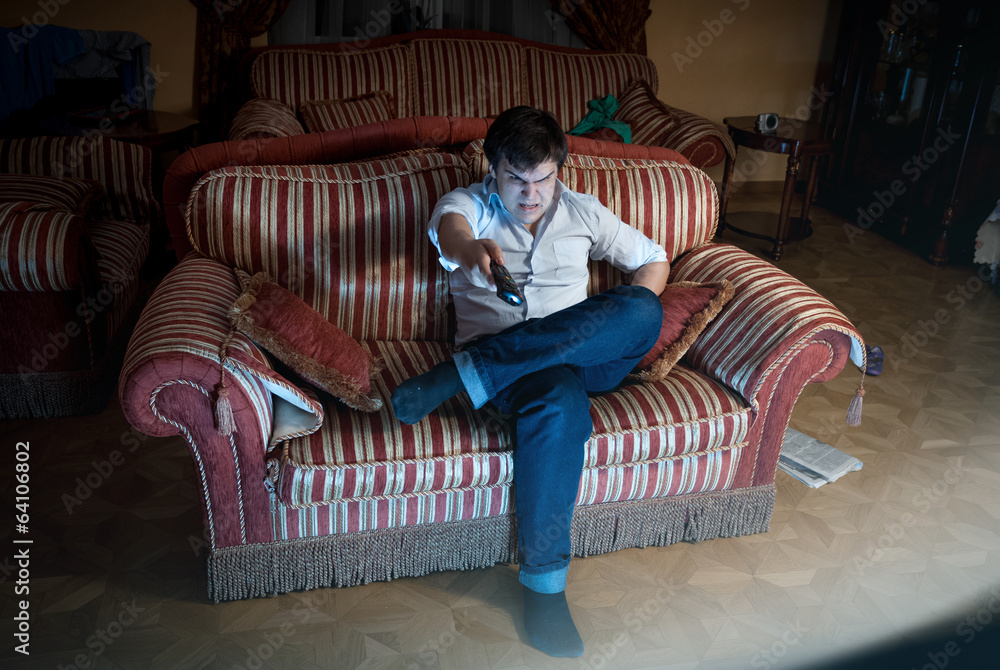 Obraz premium angry man switching TV channel while sitting on sofa