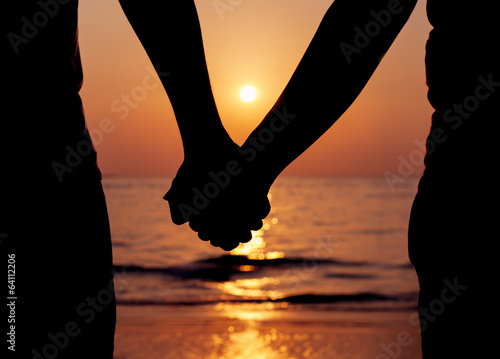 Silhouettes couples holding hands on sunset.