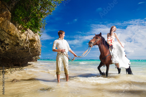 bride and groom walking with horse on a tropical beach