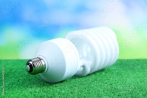 Energy saving light bulb on green grass, on bright background