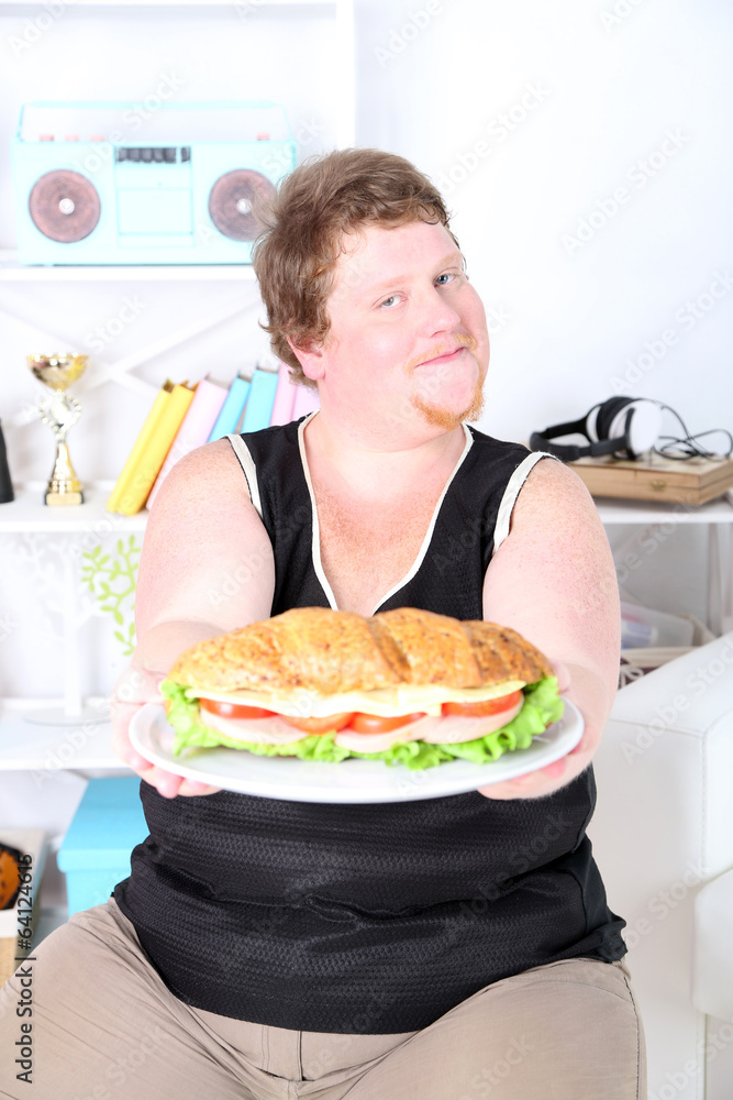 Fat man eating tasty sandwich on home interior background