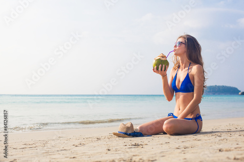 Happy young woman in blue bikini drinking coconut