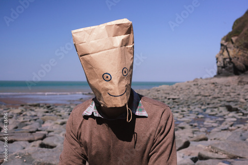 Man with paperbag over his head on the beach