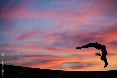 silhouetted gymnast doing a back handspring in sunset sky