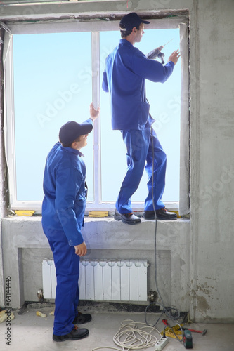 Two men in working clothes set new window frame