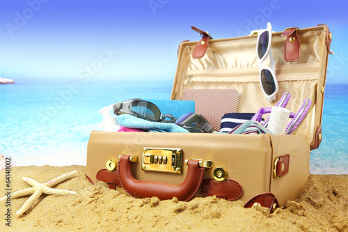 Full open suitcase on tropical beach background.