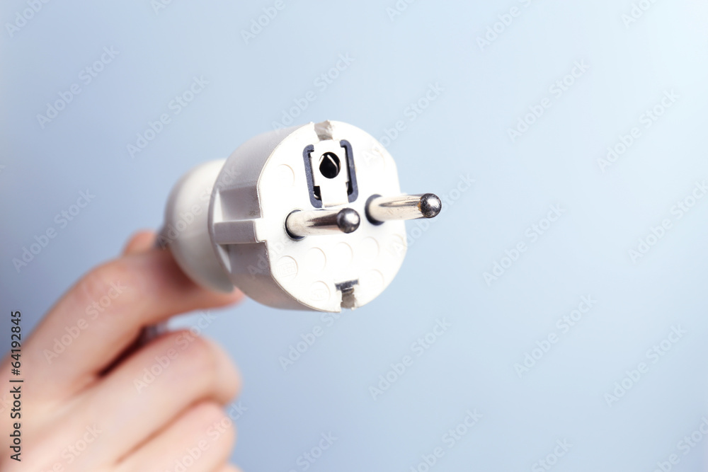 Hand holding electric plug on blue background Hand holding electric plug on blue background