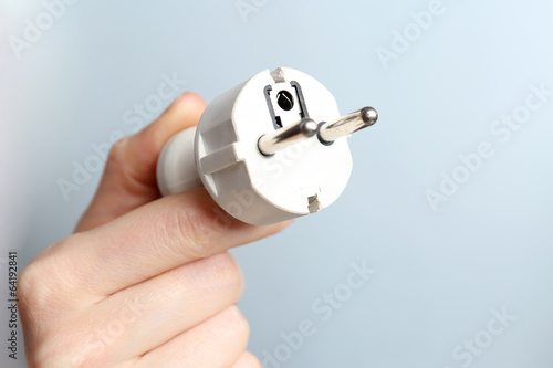 Hand holding electric plug on blue background