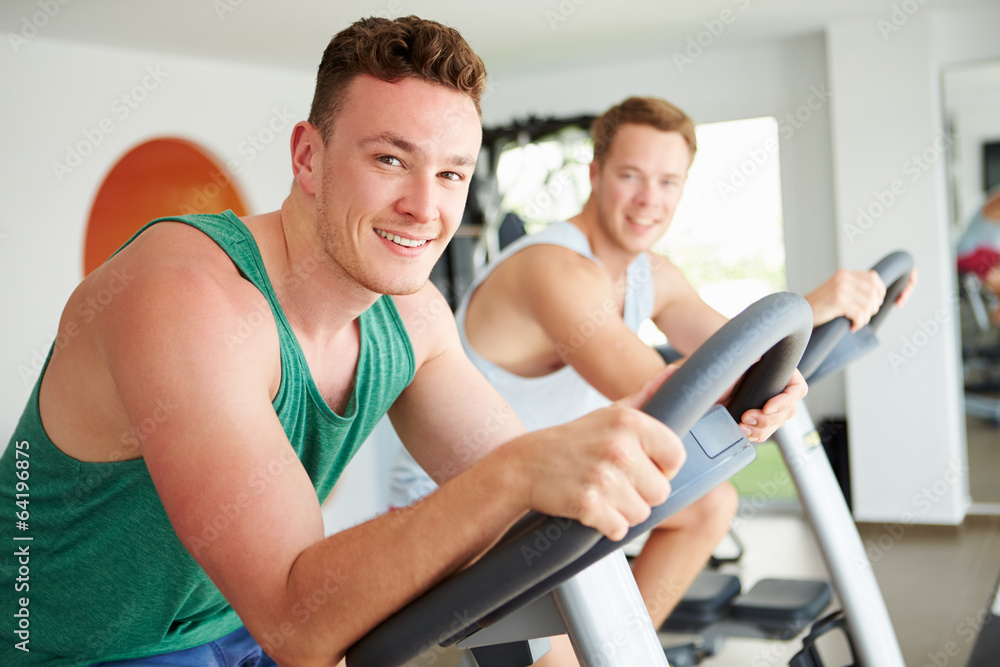 Obraz premium Two Young Men Training In Gym On Cycling Machines Together