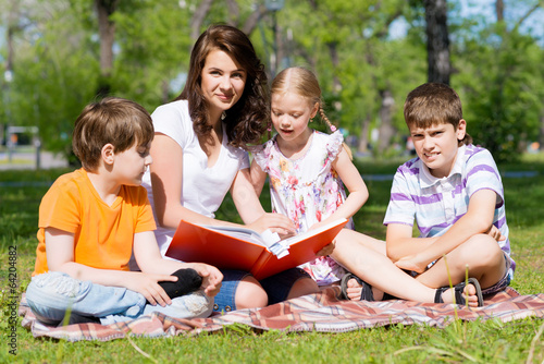 teacher reads a book to children in a summer park