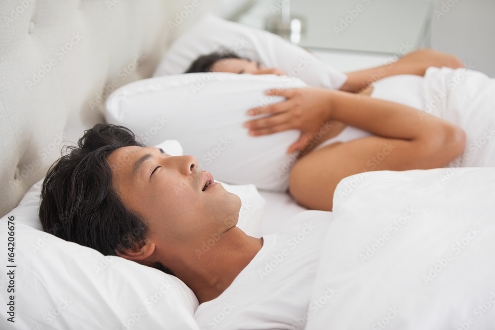 Woman covering her ears as partner is snoring loudly Woman covering her ears as partner is snoring loudly