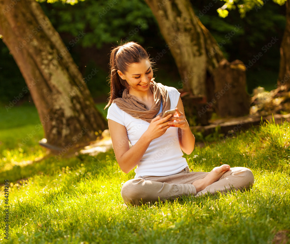 Attractive female typing sms message while sitting on grass. Attractive female typing sms message while sitting on grass.